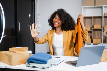 A young African American woman with afro brown hair works in a modern office, managing her online...