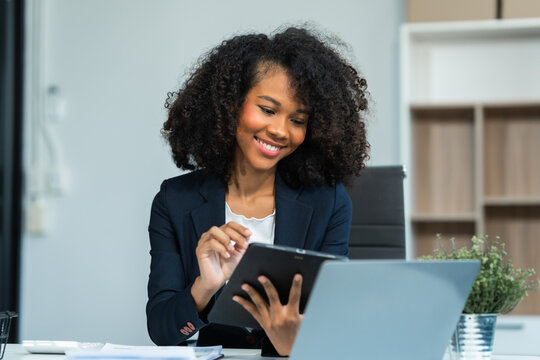 A young African American woman in a blue formal shirt with afro brown hair works as a product designer in a modern office, utilizing skills in design, CAD, CNC, and CNF.