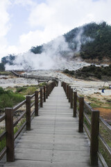 Wooden bridge leading to Sikidang Crater with white steam.