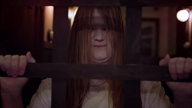 Creepy woman with ghostly white face shakes bars screaming frighteningly. Professional actress skillfully terrifies visitors in quest room