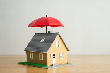 Red umbrella cover home model on wooden table with white background copy space. House, real estate, property insurance business, mortgage loan insurance concept. Insurance is risk control management. © pla2na