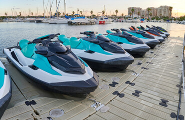 Rental jet skis parked in a row on a floating dock in a marina at sunset. Concept of water sports...