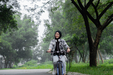 Young cheerful hijab woman, wearing casual flannel riding bicycle bike on sidewalk in city enjoying...