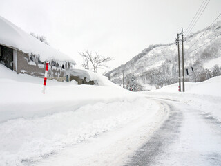 Winter snowy white countryside road, house with big snowdrift on the roof,   distant mountains, nature of Yamagata, Japan