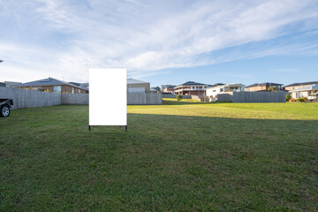 Blank white mockup template of a real estate sign on a vacant land lot with some new and modern Australian suburban homes in the background. Empty advertisement board with copy space.