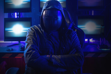 Hacker wearing a hoodie and mask to conceal his identity stands with his arms crossed in front of a...