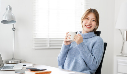 Happy young woman wearing sweater drinking a cup of  coffee at home office,  sitting in living room.