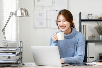 Beautiful lady wearing  sweater holding coffee cup working on laptop,  sitting at home office.