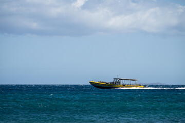 Medium yellow tourist boat cruising on a calm pacific ocean on a sunny day, water, sky, and horizon, Maui, Hawaii

