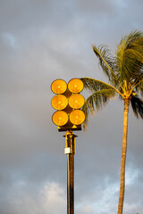 Bright yellow tsunami sirens and palm trees against a cloudy sky at sunset, pacific ocean tidal wave warning system on Maui, Hawaii
