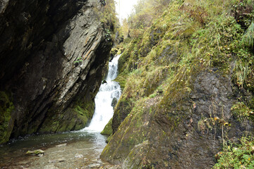 A stepped cascading waterfall flows in a rapid stream from a crevice in the mountains on a cloudy autumn day.