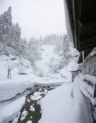 Yamagata winter scenery with waterfall on Mountain river with big fluffy snowdrifts on the stones and pine forest on the hill