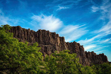 Craggy cliffs blue sky clouds green trees, rugged outdoor wilderness scene, outdoor serene panoramic landscape