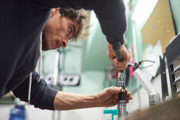 Young hispanic man servicing a bicycle in his repair shop. Real people at work. Composition with...