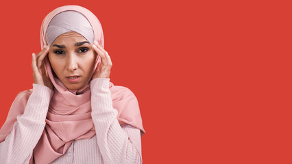 Migraine attack. Headache disorder. Tension fatigue. Disturbed sad woman in headscarf massaging head temples suffering from pain isolated on red empty space background.