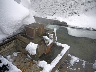 Ashiyu or japanese onsen  hot spring  foot bath on Mountain river bank with  snowdrifts, Ginzan...