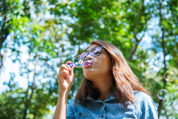 Adorable happy cute girl playful foam bubbles in green playground in summer outdoors. Funny Cheerful girl in the park happiness times. Bubbles blowing soap playful in nature park.