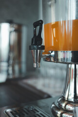Fresh orange in a large glass jug, prepare as self-service station in breakfast buffet food line. Close up and selective focus at the tap valve