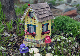 Cute fairy doll house with spring flowers outside in the garden. Lovely miniature for greeting cards, wedding or birthday concept, real estate, downsizing, home ownership