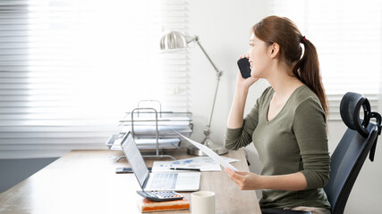 Businesswoman in casual wear working  on document at her home office, using mobile phone talking with her colleagues
