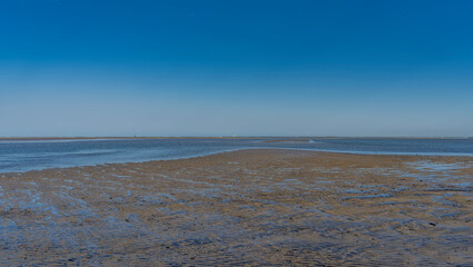 The sandy bottom was exposed at low tide. Pools of water among wavy ridges and bumps. The blue...