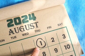 Hand pointing on August 1 2024 date on calendar flat lay in blue background. First day of August...
