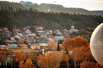 Tbilisi in autumn, showcasing city's dense residential areas with backdrop of colorful trees...