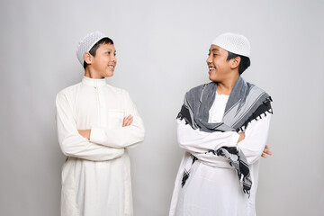 Two Muslim boys in white robe smiling while looking at each other isolated on white background