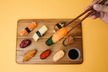 Sushi platter. A selection of raw fish and rice snacks with chopsticks on yellow background.