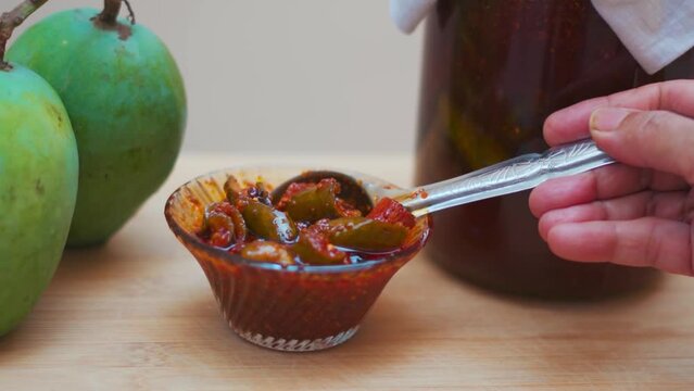 Close up shot of Indian woman hand taking Mango Pickle with spoon. Indian handmade organic sweet pickle. Aam Achar delicious homemade food.