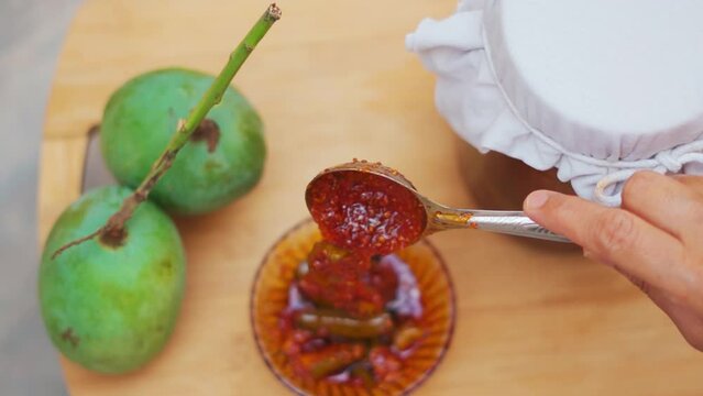 Top down shot of mango pickle in bowl with raw mangoes and jar in background. Authentic homemade pickle. Gujarati food.