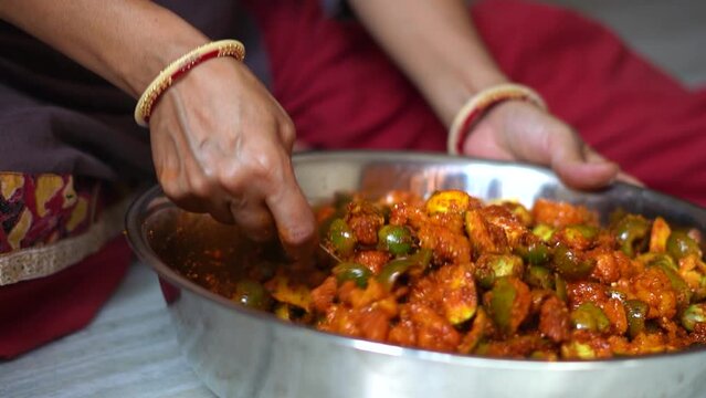 Hands of Indian woman wearing bangles mixing raw mangoes with spices to make Mango pickles. Homemade organic pickle. Female preparing food in kitchen. An Indian housewife making pickle, household work