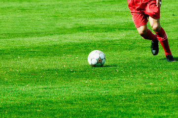 legs of a soccer player in red dress on green turf, with the ball, in action, dynamic