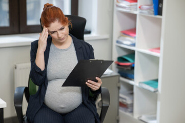 Pregnant woman reading documents on a paper tablet in the office. 