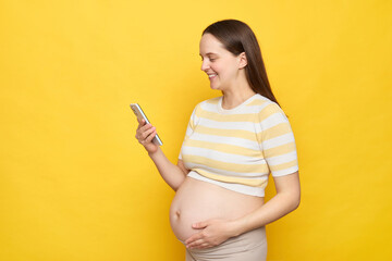 Smiling happy positive young Caucasian pregnant woman dressed in top posing against bright yellow...