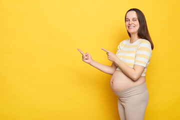 Smiling cheerful Caucasian pregnant woman in casual clothing posing isolated over yellow background...