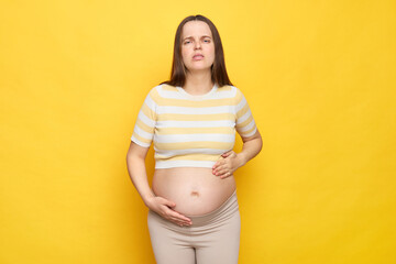 Sick Caucasian pregnant woman in casual clothing posing isolated over yellow background feeling...