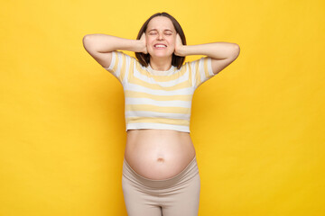 Irritated brown haired pregnant woman with bare belly posing isolated over yellow background...