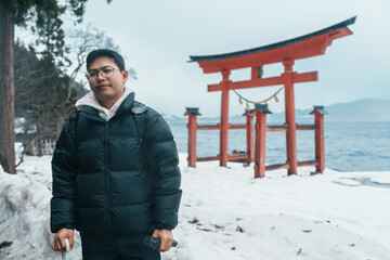 man  tourist sightseeing Japanese Torii gate  Shrine and lake Tazawa. Traveler travel in Semboku...