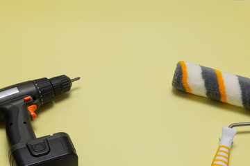 Electric screwdriver and paint roller on a yellow background. Construction tools for repair. Flat...