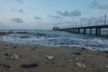 waves with foam at the beach with a long jetty at the sea
