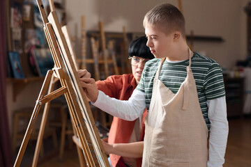 Side view portrait of young boy with disability drawing picture in art therapy class standing by...