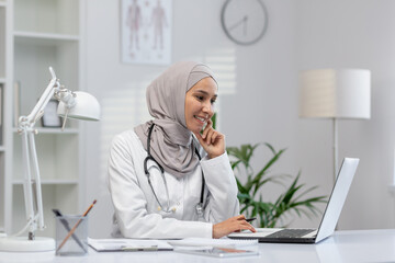A cheerful Muslim female doctor in hijab engages with a patient online, sitting confidently at her...