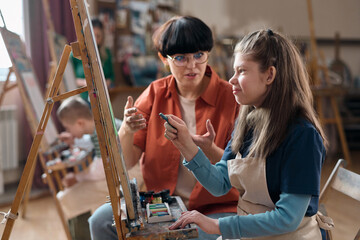 Side view portrait of smiling girl with disability painting on easel while enjoying art class with...