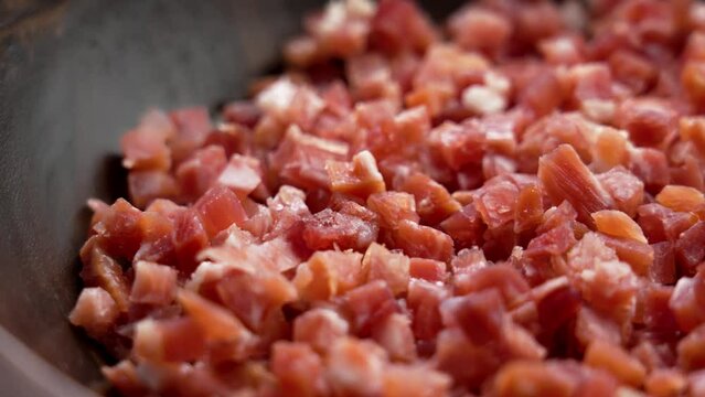 Traditional Spanish jamon cubes in wooden bowl close up. Meat cooking ingredient. Rotation