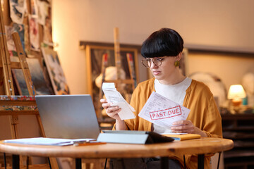 Portrait of female artist sorting bills and taxes while managing small business