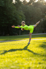 A woman in a neon yellow outfit is doing a yoga pose on a grassy field