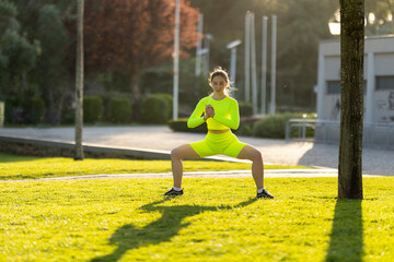 A woman in a neon yellow outfit is doing a yoga pose in a park
