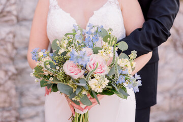 A bride and groom are cuddling, and she holds a bouquet of pretty flowers with pink and purple...