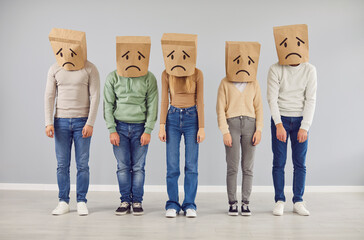 Naklejka premium Diverse people group wears paper bags on their heads, each adorned with a drawn sad face. This thought provoking portrait captures a shared emotion and a sense of collective experience.